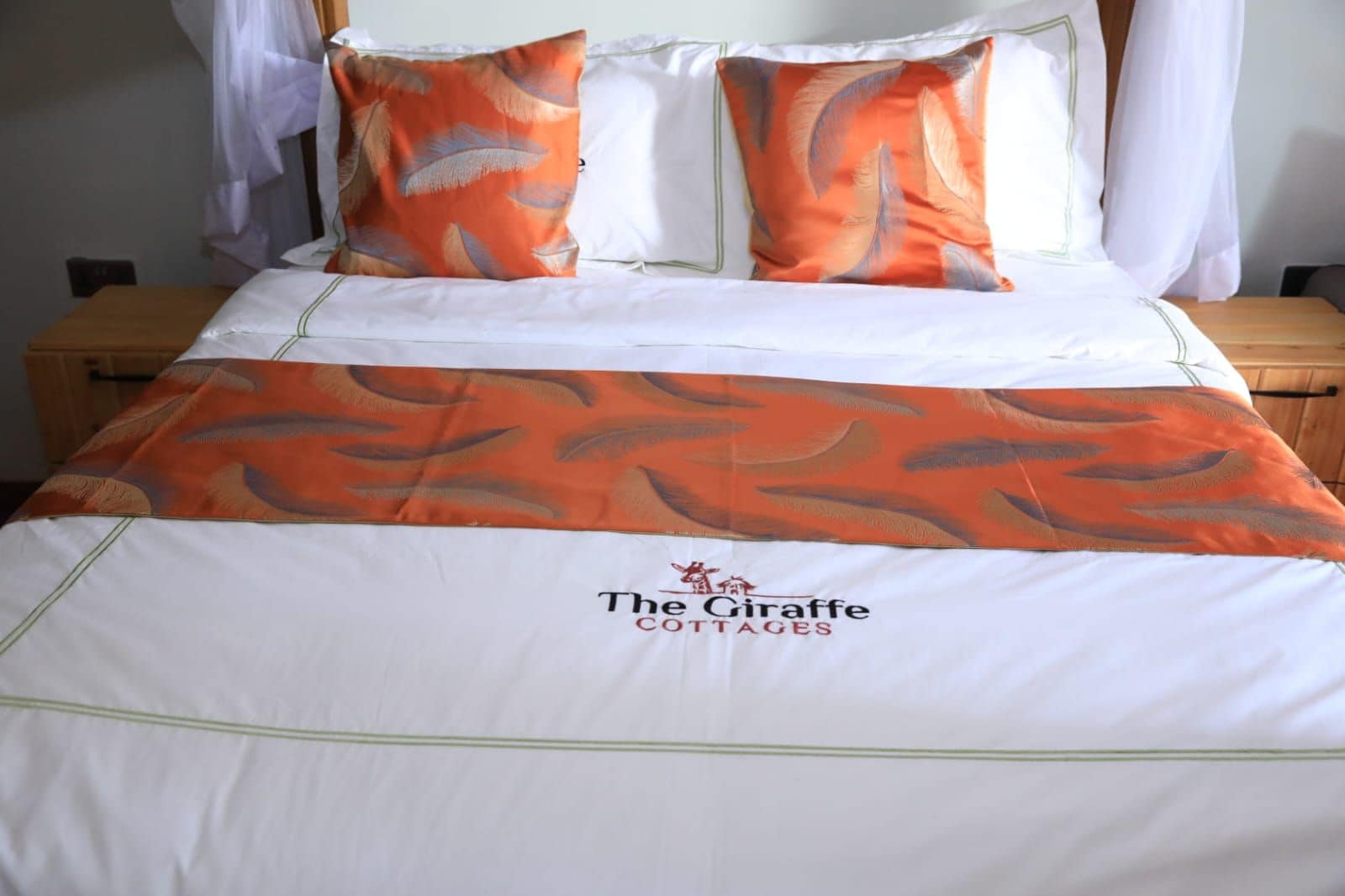 Ein Bett mit einer weißen und orangefarbenen Tagesdecke, zwei Kissen und das Logo von The Giraffe Cottages.