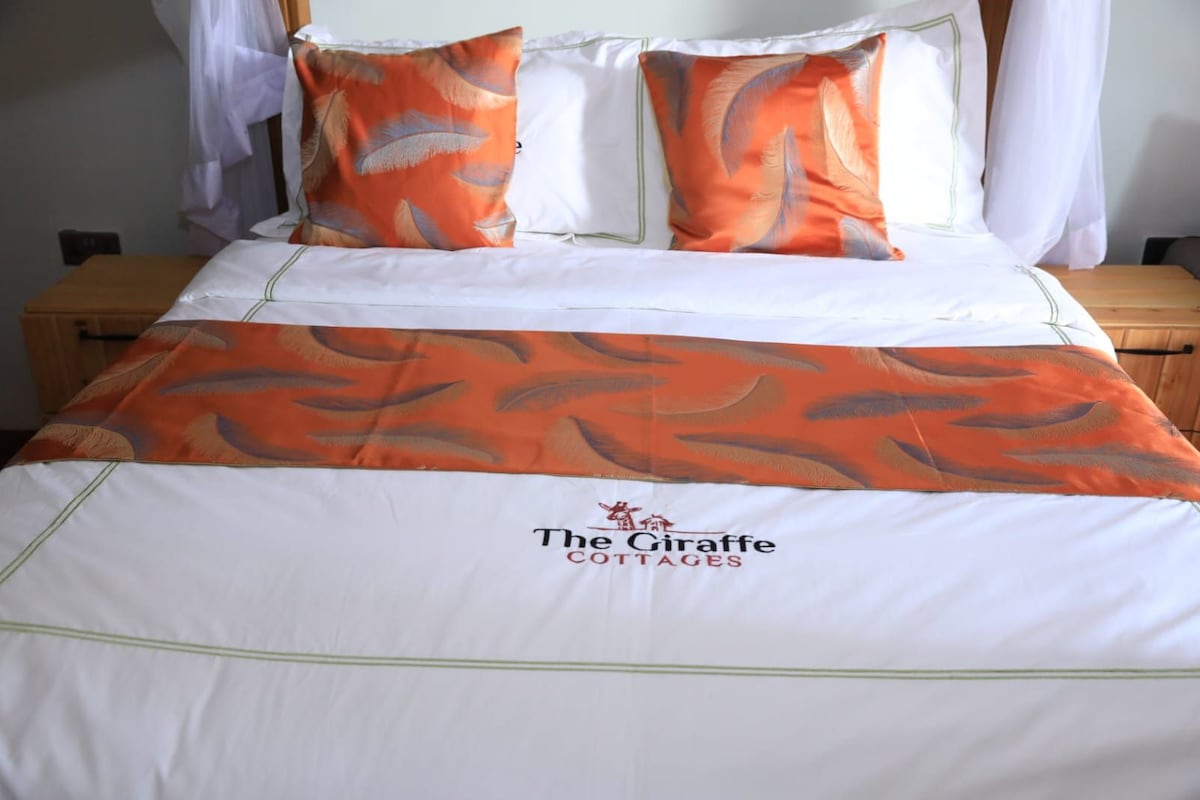 A bed with a white and orange bedspread, two pillows, and a logo for The Giraffe Cottages.