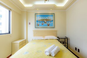 Ein Hotelzimmer mit Bett, einem Gemälde von Booten auf dem Wasser, einem Fenster und einem Nachttisch.