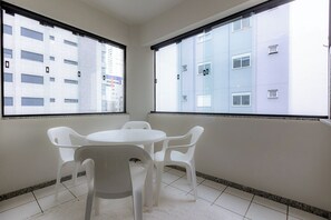 Ein Zimmer mit einem weißen Tisch und vier Stühlen, großen Fenstern mit Blick auf ein Gebäude und einem gefliesten Boden.
