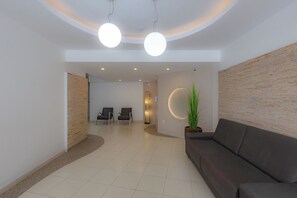 Ein moderner Empfangsbereich mit gewölbter Decke, zwei Pendelleuchten, einer Rezeption, einer Sitzecke mit Sofa und einem Blumentopf.