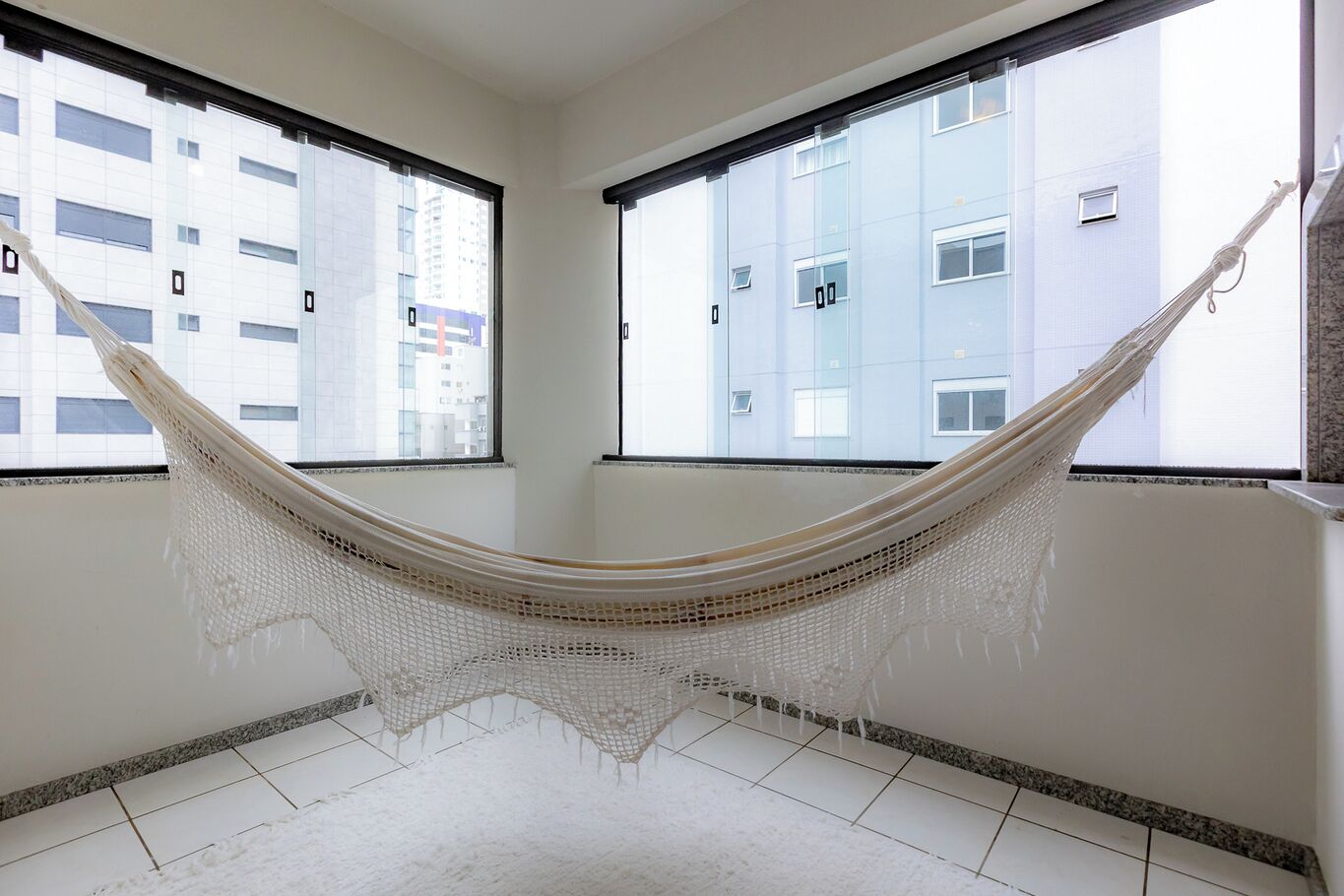 A room with a hammock, large windows, and a view of a building.