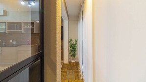 Ein schmaler Flur mit Holzboden, einem Blumentopf und einem durch eine Glastür einsehbaren Küchenbereich.