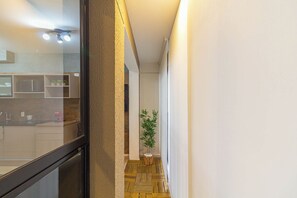Ein schmaler Flur mit Holzboden, einem Blumentopf und einem durch eine Glastür einsehbaren Küchenbereich.