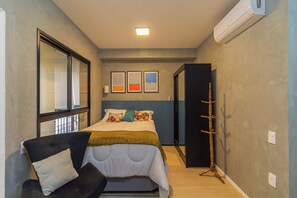 Ein Schlafzimmer mit Bett, Stuhl, Kleiderhaken und Fenster.