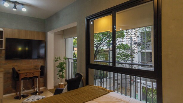 Ein Schlafzimmer mit großem Fenster, Fernseher, Schreibtisch und Stuhl.