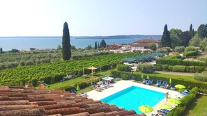 Ein Poolbereich mit Liegestühlen und Sonnenschirmen, umgeben von Weinbergen und Blick aufs Meer.