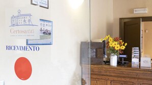 En receptionsdisk med en vas med blommor, ett inramat certifikat och en skylt på väggen med texten ”RICEVIMENTO”.