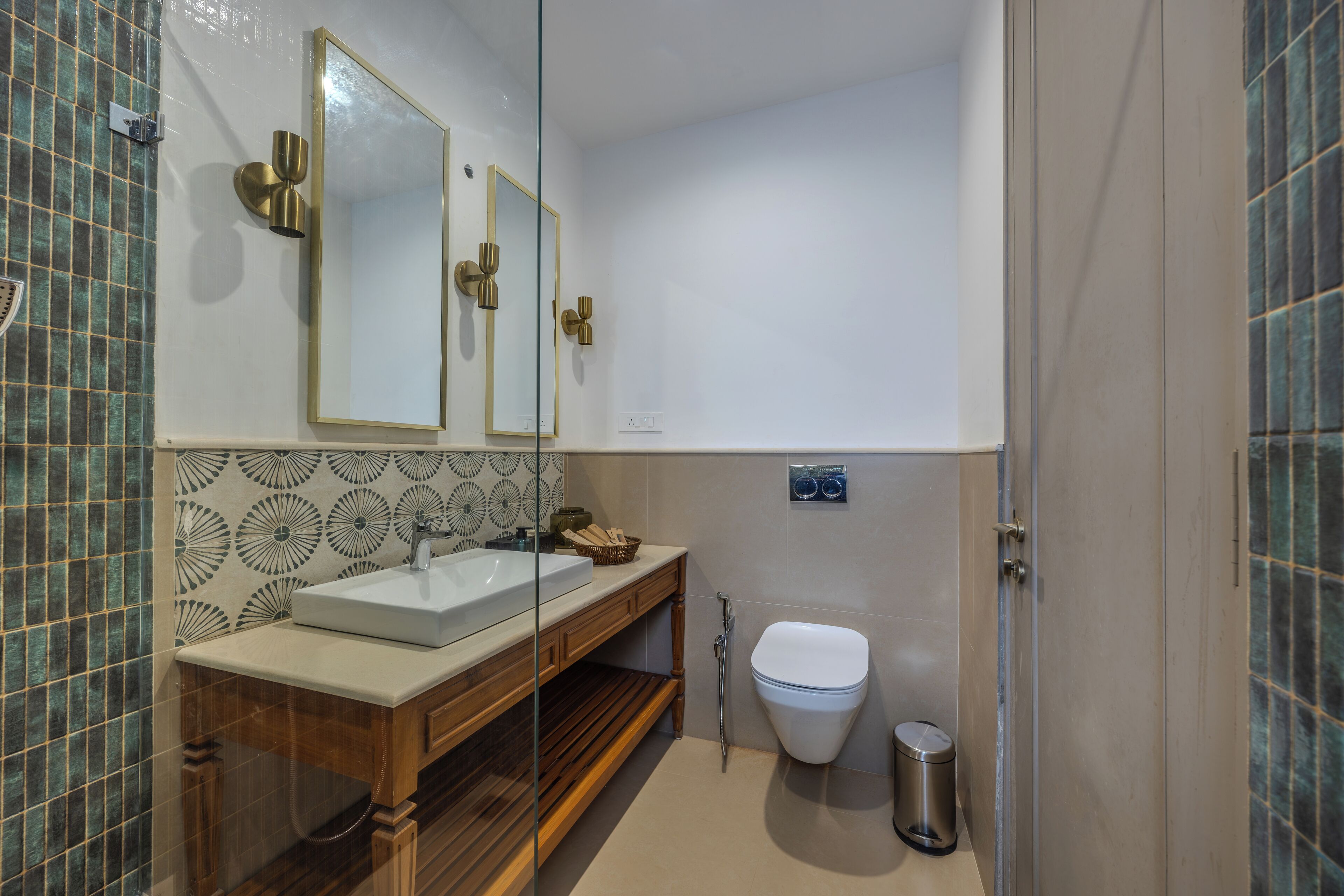 Une salle de bain avec un meuble-lavabo en bois, un lavabo blanc, un miroir avec un cadre doré, des toilettes blanches et une poubelle.