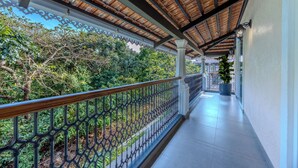 A covered balcony with a metal railing, potted plants, and a view of greenery.