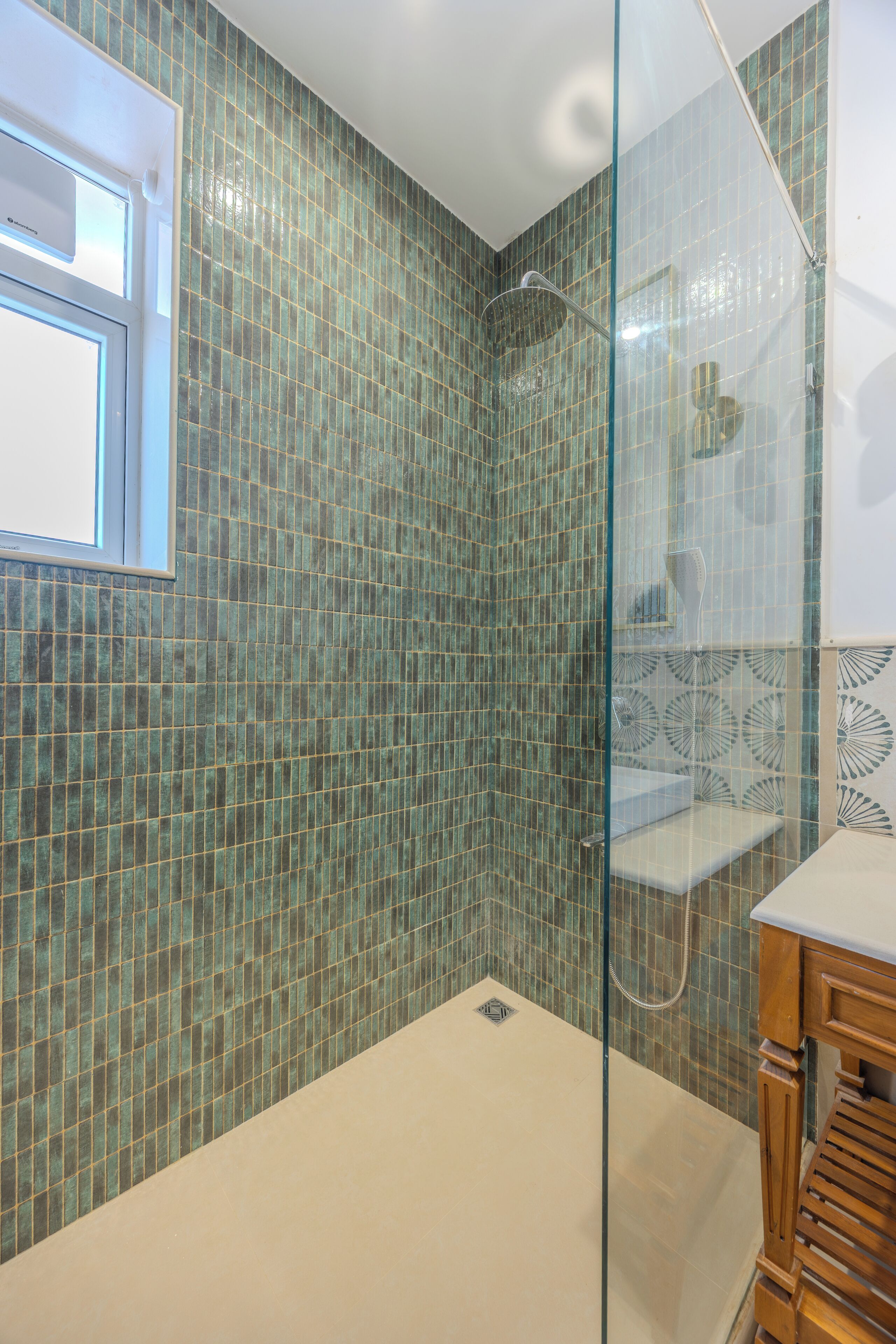 Un baño con ducha de vidrio, paredes con azulejos, ventana y tocador de madera.