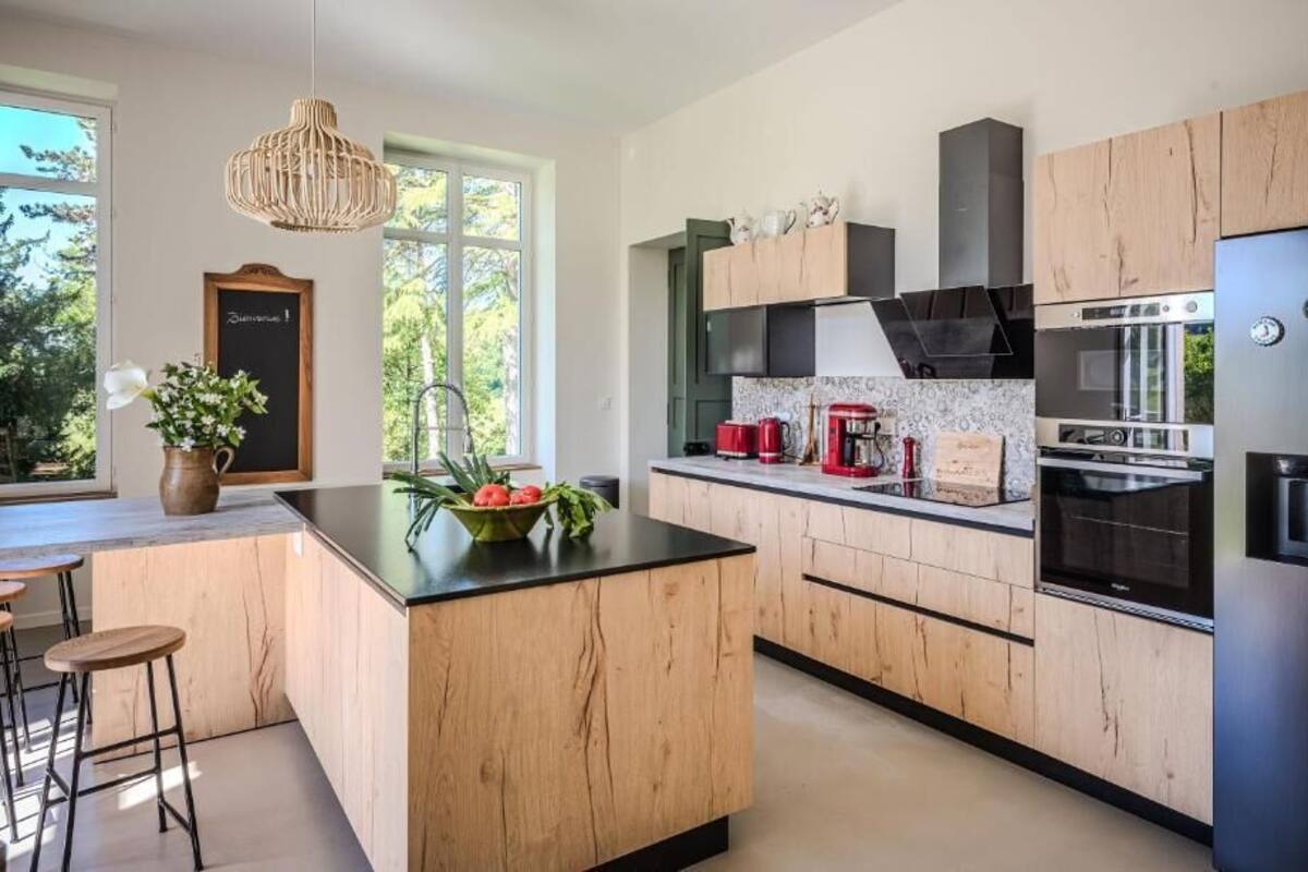 A modern kitchen with wooden cabinets, a central island, a built-in oven, and a stainless steel refrigerator.