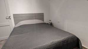Ein Schlafzimmer mit Bett, Nachttisch, Lampe und einer Tür.