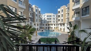 Ein moderner Apartmentkomplex mit einem zentralen Schwimmbad, Balkonen und umgebender Bepflanzung.