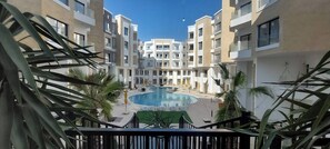 Ein moderner Apartmentkomplex mit einem zentralen Schwimmbad, Balkonen und umgebender Bepflanzung.