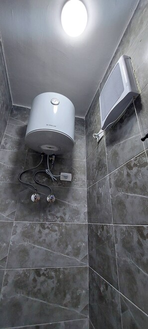Ein Badezimmer mit Wand-Klimaanlage, Deckenleuchte und Warmwasserbereiter.