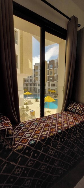 Ein Hotelzimmer mit Bett, Vorhängen und Blick auf ein Schwimmbad sowie Gebäude.