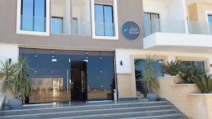 Ein moderner Hotelzugang mit Glasfassade, einem Schild für Aqua Infinity Resort und einer Treppe zum Eingang.