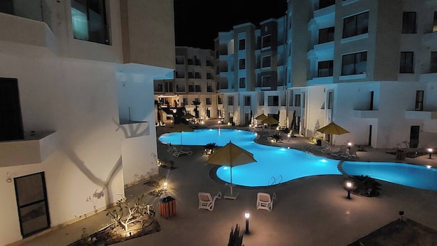 Ein Nachtblick auf einen Hotelinnenhof mit mehreren Pools, Liegestühlen und Sonnenschirmen.