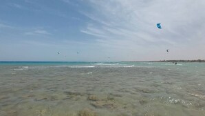 Ein Strand mit klarem Wasser und Menschen, die Drachen steigen lassen.