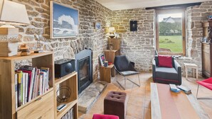 A cozy living room with a stone wall, a fireplace, a bookshelf, a sofa, and a view of the outdoors. - Beautiful house for 8 with garden – Sea view (Penmarch)
