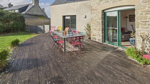 A patio with a table and chairs, a stone building, and a glass door leading to an interior space. - Beautiful house for 8 with garden – Sea view (Penmarch)