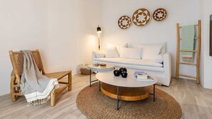 A modern living room with a white sofa, a round coffee table, a wicker chair, and a floor lamp. - Julies, Sunset Bliss Apartment – Agia Anna (Naxos)
