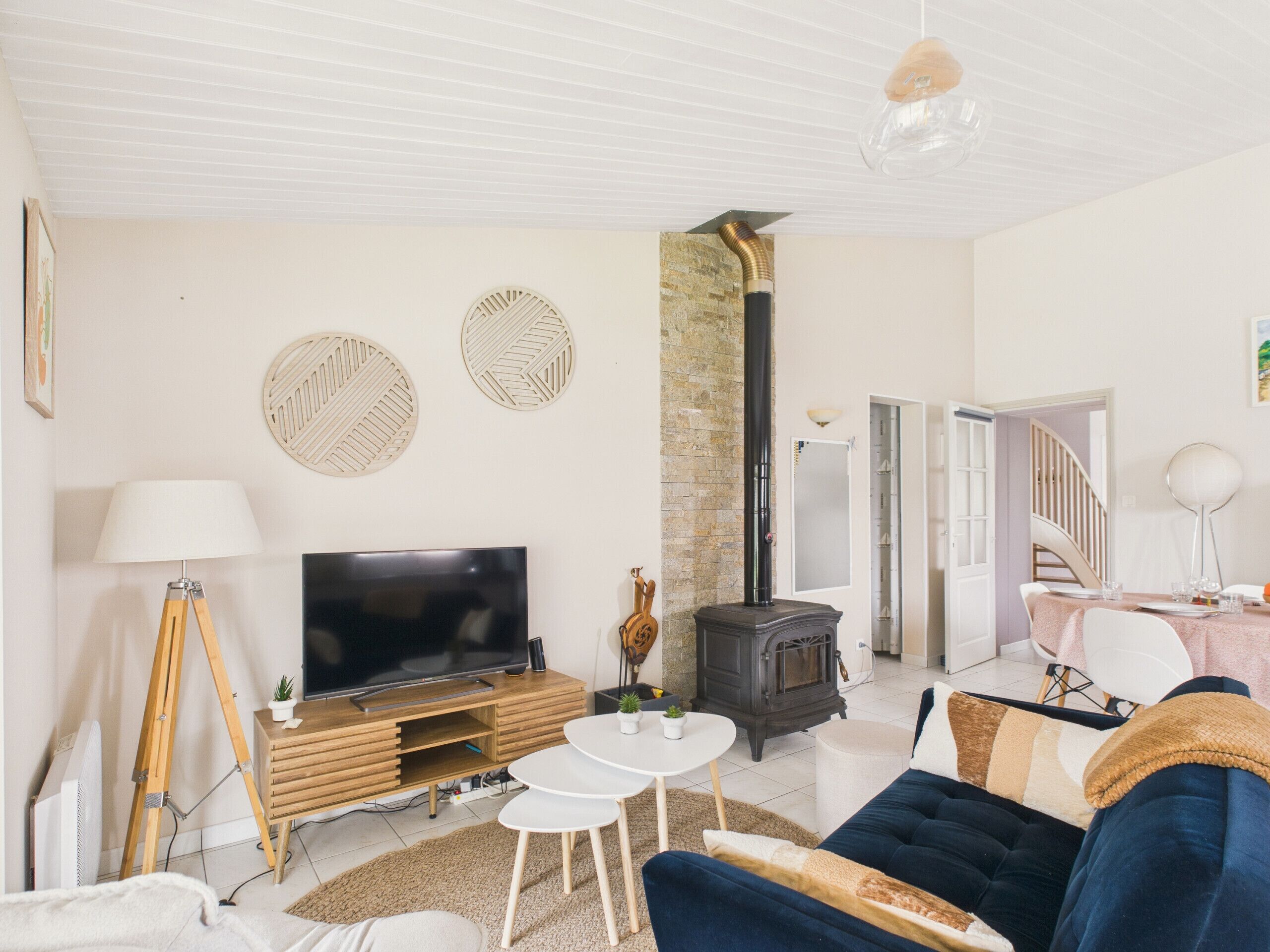 Un salon avec un téléviseur, un meuble de rangement en bois, un mur en pierre, un poêle noir et un canap é bleu.