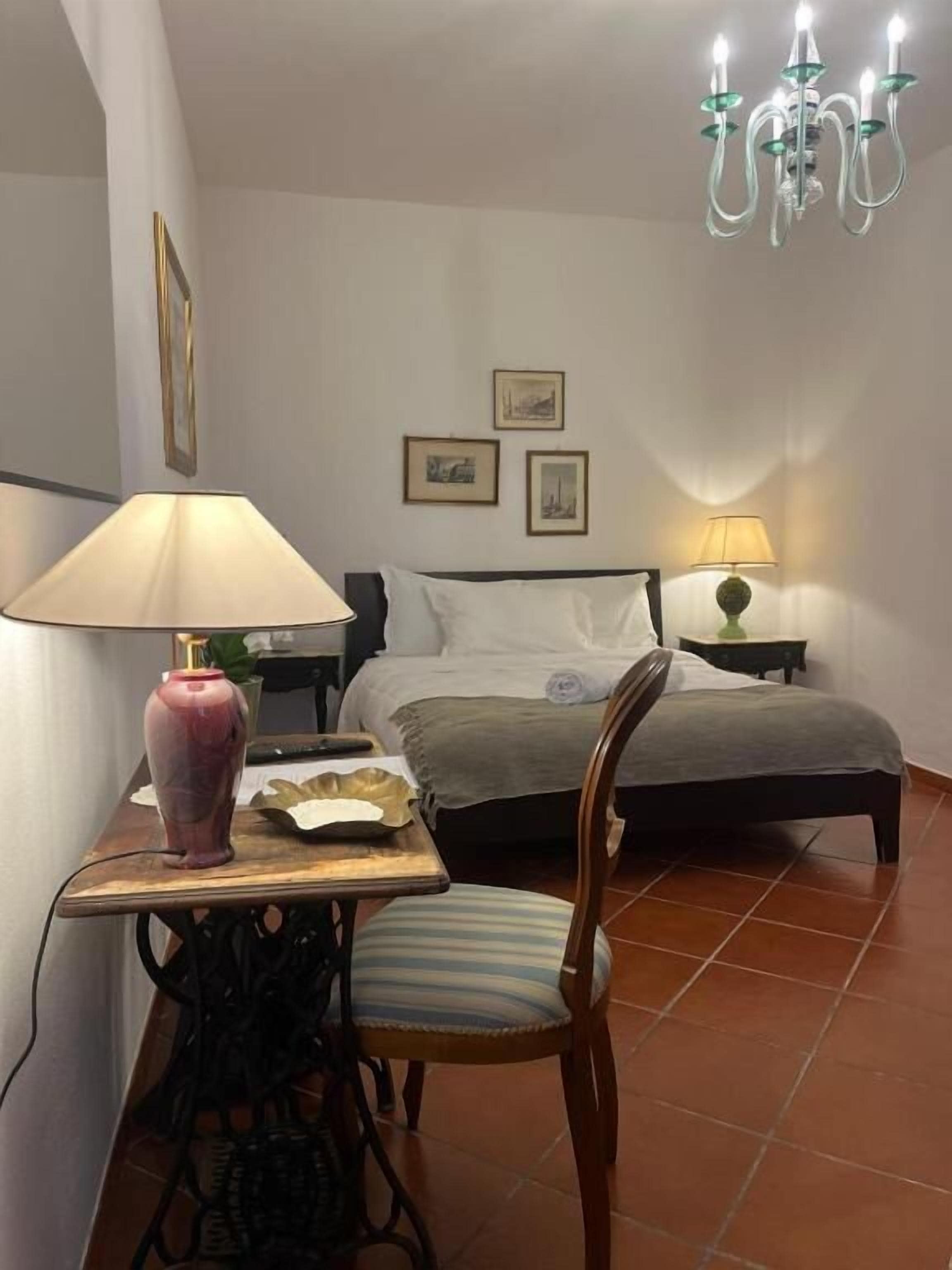 Une chambre à coucher comprenant un lit, des tables de chevet, une chaise, une table avec une lampe et un lustre.