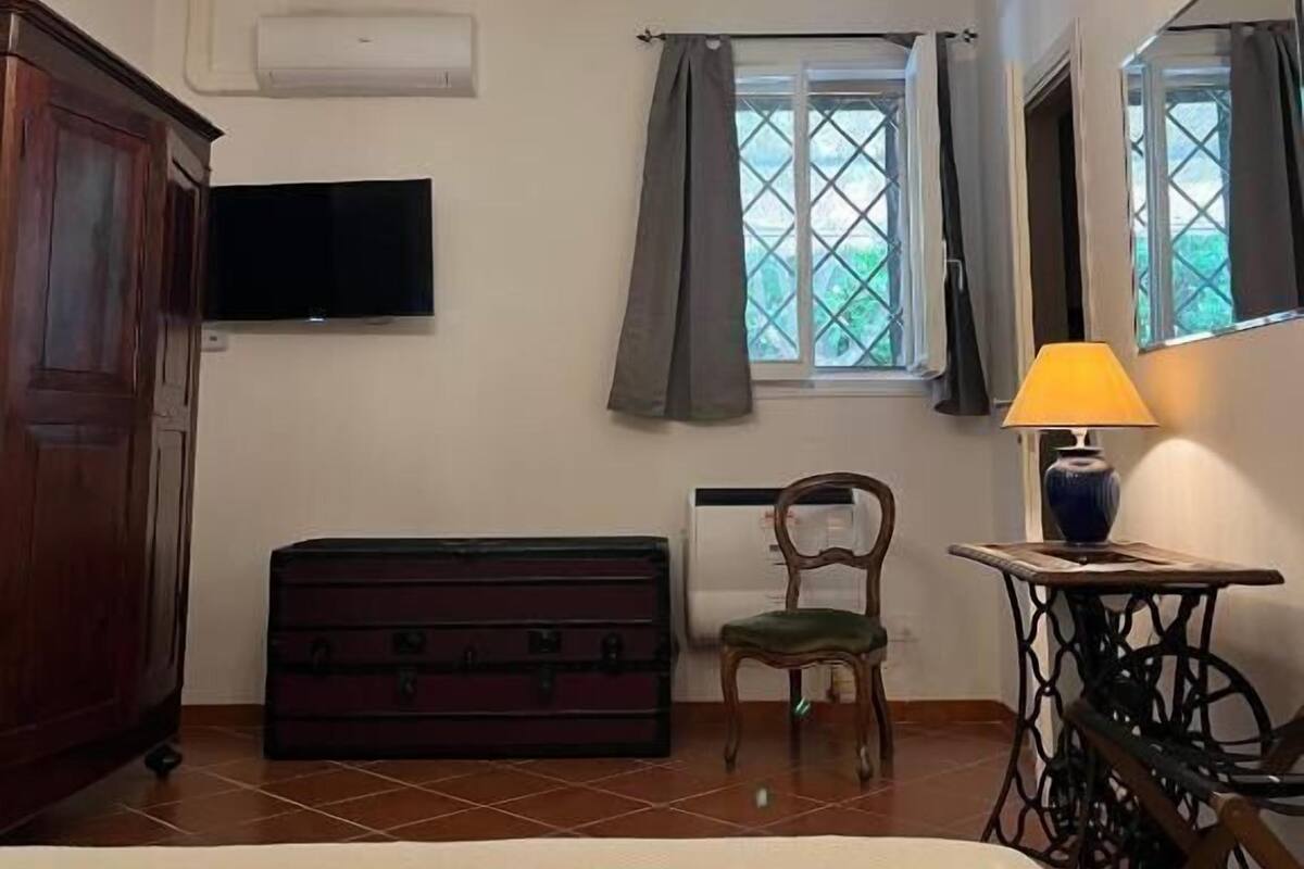 Quarto com lustre, televisão, janela com cortinas, cama, cômoda e abajur.