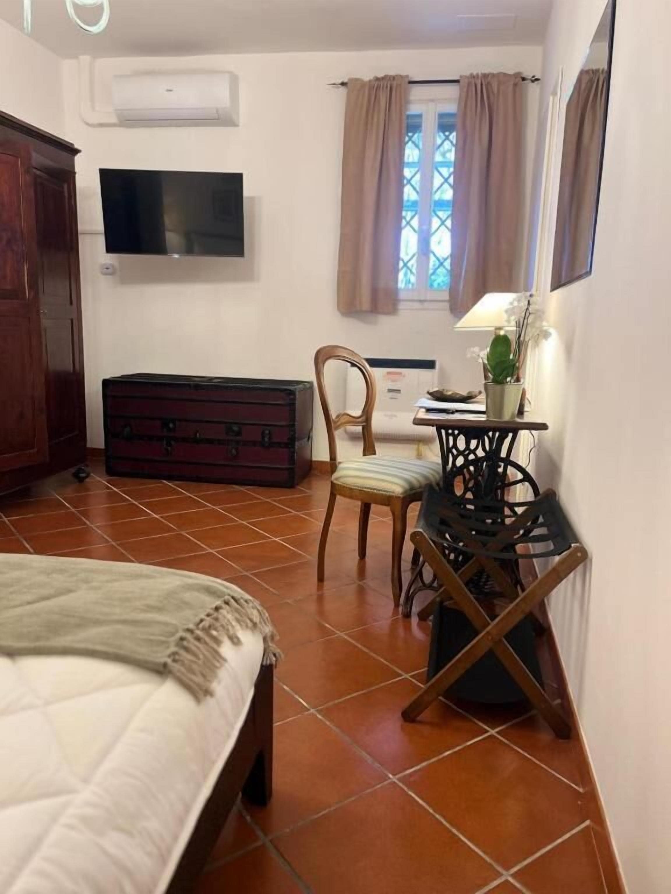 Un dormitorio con cama, armario de madera, televisor, escritorio con lámpara y ventana con cortinas.