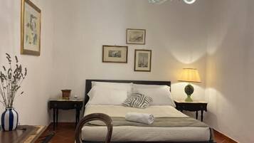 A bedroom with a bed, a chair, a table, a lamp, and a chandelier.