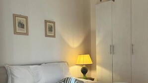 A neatly made bed with white linens, a striped pillow, and a rolled towel. There is a nightstand with a lamp and a framed picture on the wall. - Levante Camere (Calderara di Reno)
