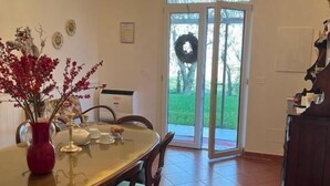 A dining area with a chandelier, a table set for four, and a view of a garden through glass doors. - Levante Camere (Calderara di Reno)