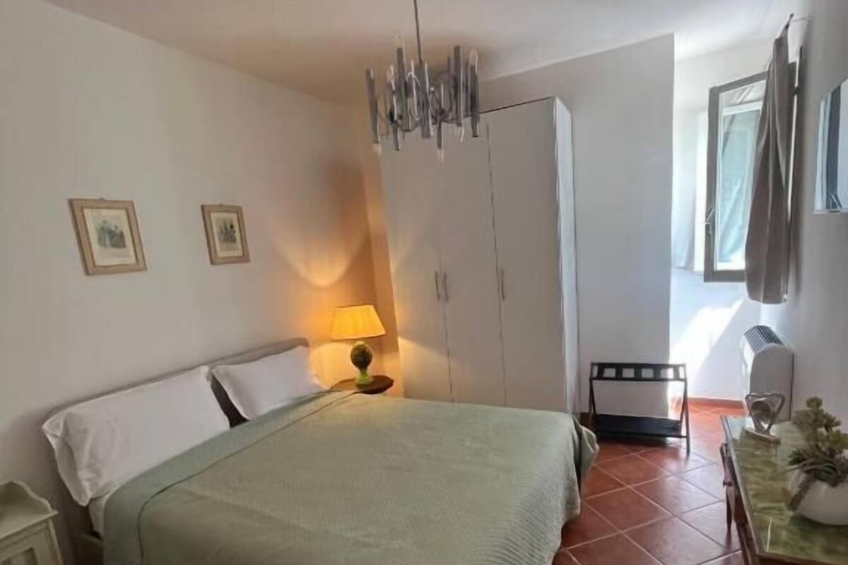 Quarto com cama, mesa de cabeceira, luminária, guarda-roupa e janela.