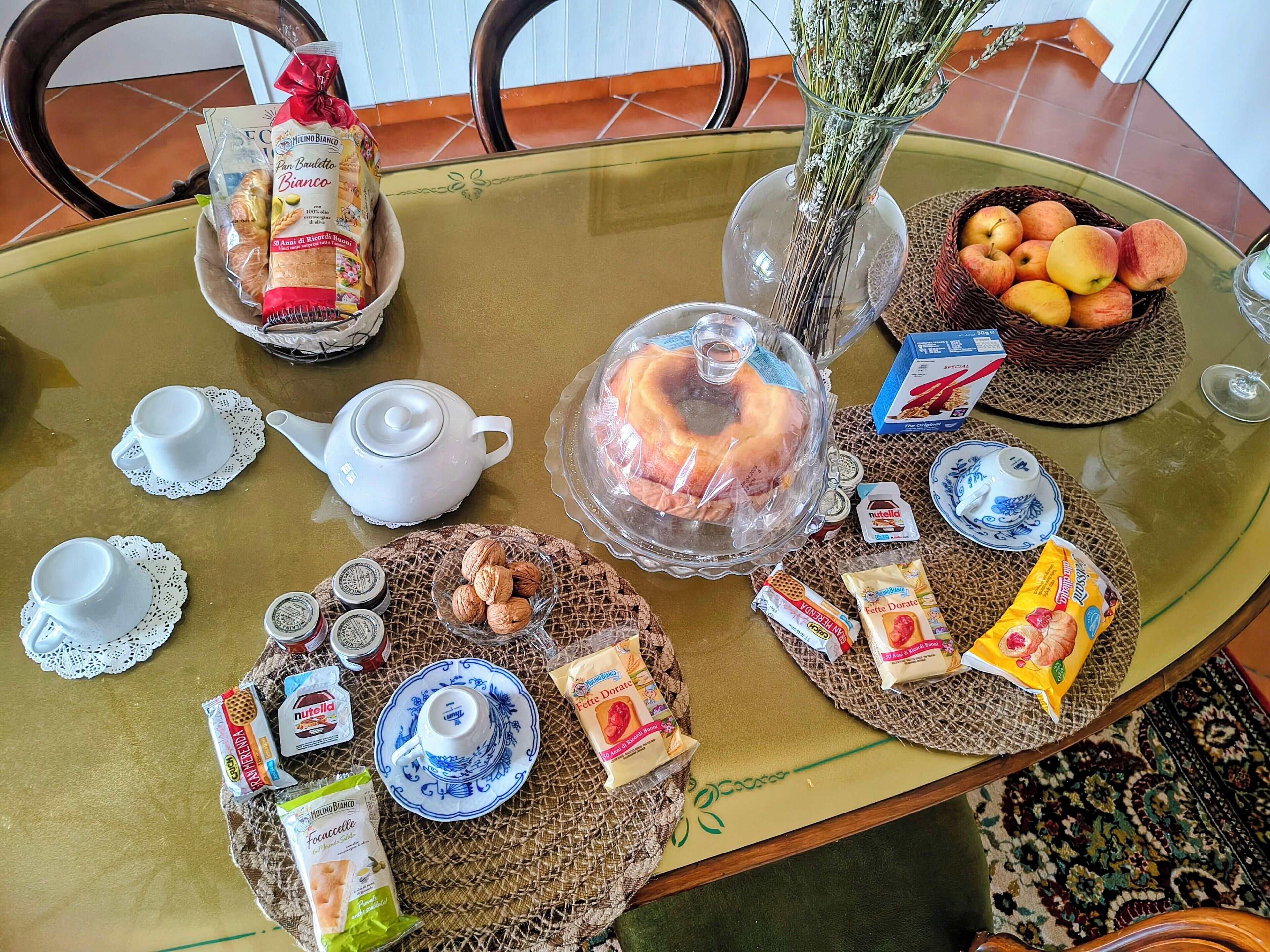 A breakfast table with various food items, a teapot, and a vase with flowers.
