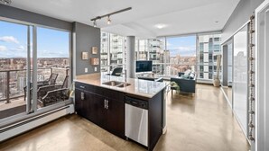 A modern kitchen with a large island, a dining area, and a view of the cityscape. - DT Views | UG Park | Walk to Saddledome |AC (Calgary)