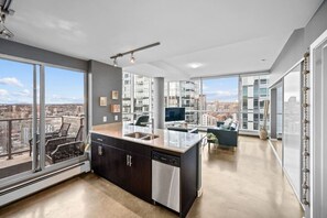 A modern kitchen with a large island, a dining area, and a view of the cityscape. - DT Views | UG Park | Walk to Saddledome |AC (Calgary)