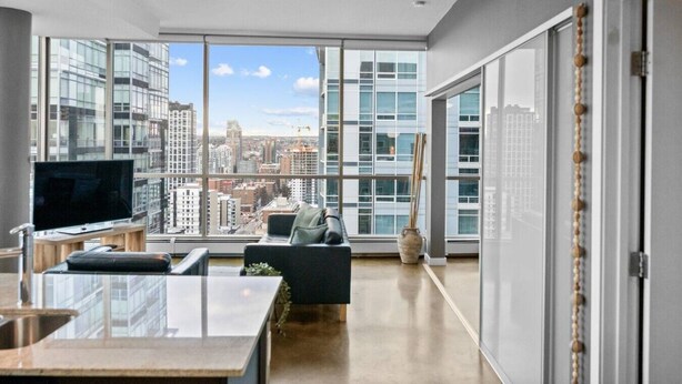 A modern living room with a large window, a flat-screen TV, a sofa, and a coffee table. - DT Views | UG Park | Walk to Saddledome |AC (Calgary)