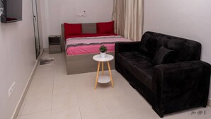 A bedroom with a bed, a black sofa, a small table with a plant, a TV, and a painting on the wall. - Maison Recla (Lomé)