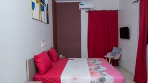 A bedroom with a bed, a chair, a small table, a TV, and a wall-mounted air conditioner. - Maison Recla (Lomé)
