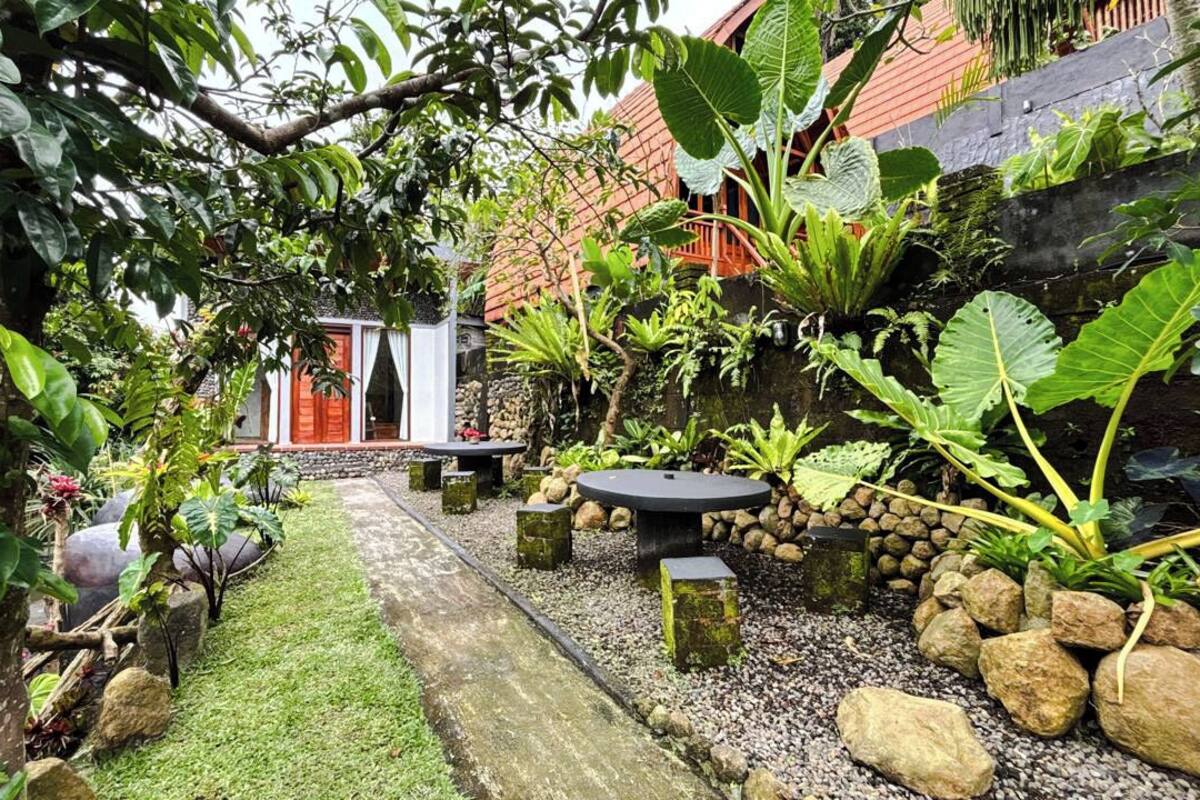 A garden with a stone pathway, seating area, and a small building with a red door.