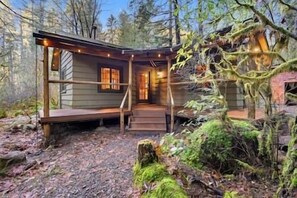 A cabin with a porch, wooden exterior, and a window with curtains.