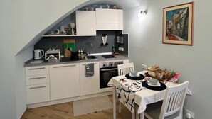 A compact kitchen with a dining area, a painting on the wall, and a wooden floor. - Cà DE SAN SCì (Sanremo)