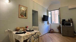 A dining area with a table set for two, a television mounted on the wall, and a window with curtains. - Cà DE SAN SCì (Sanremo)