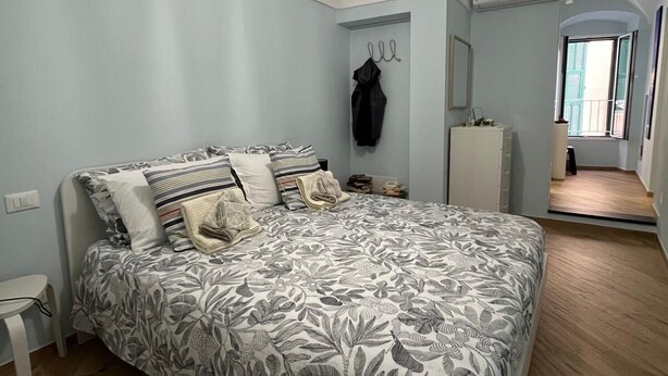 A bedroom with a bed, a hanging light fixture, a coat rack, and a window. - Cà DE SAN SCì (Sanremo)