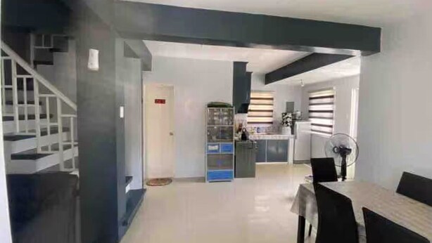 Una cocina moderna con una isla central, un área de comedor con una mesa y sillas, y una escalera que sube a un nivel superior.
