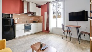 Ein kompakter Wohnraum mit Küchenzeile, einem Essbereich mit Tisch und Stühlen sowie einem an der Wand montierten Fernseher.