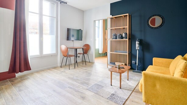 Ein modernes Wohnzimmer mit einem gelben Sofa, einem HolztV-Schrank und einem Essbereich mit zwei Stühlen.