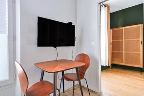 Ein Zimmer mit Holztisch, Stühlen, einem flachbildfernseher an der Wand und einem Holzschrank.